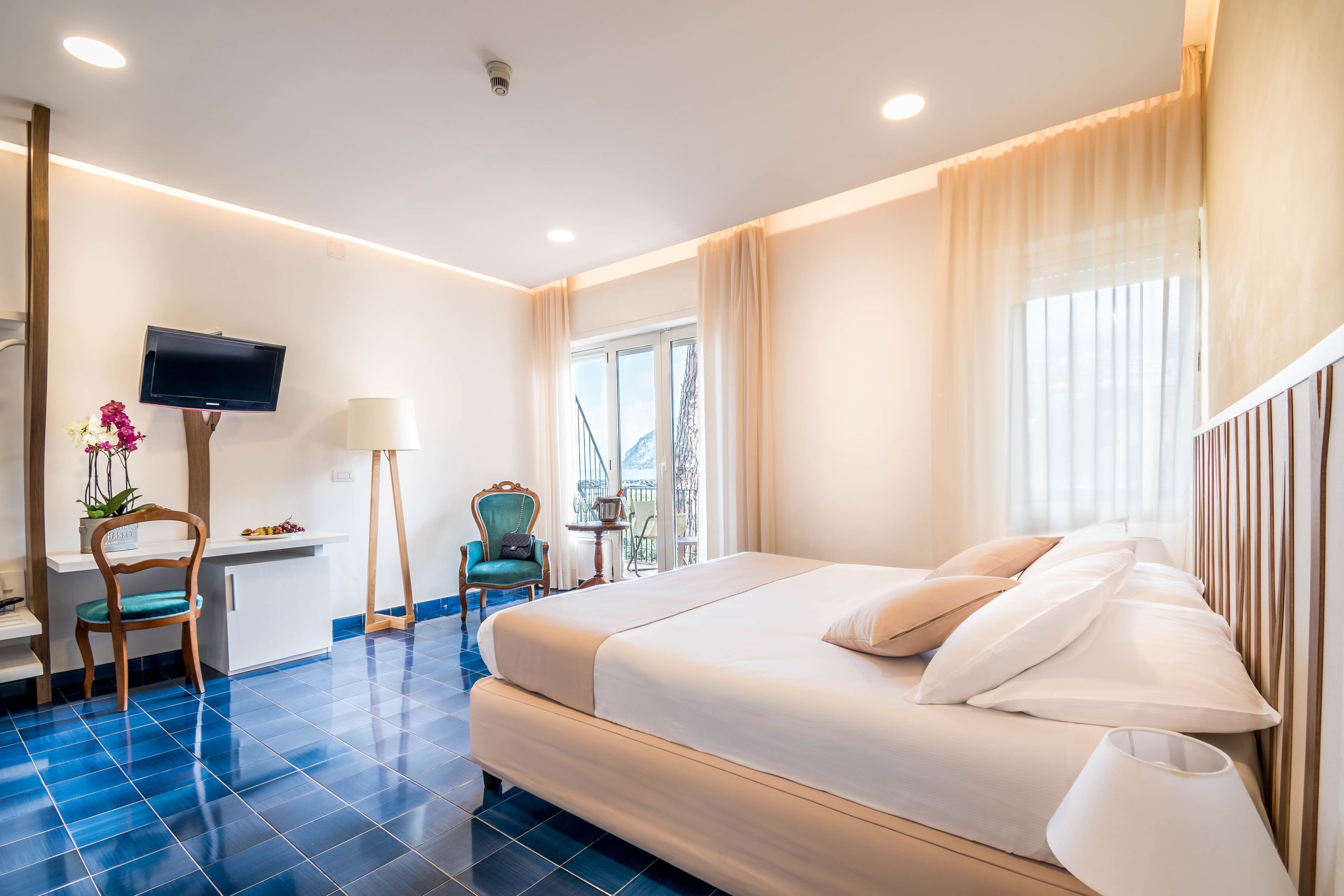 A hotel room with a bed, a desk, a chair, a TV, and a window with curtains.