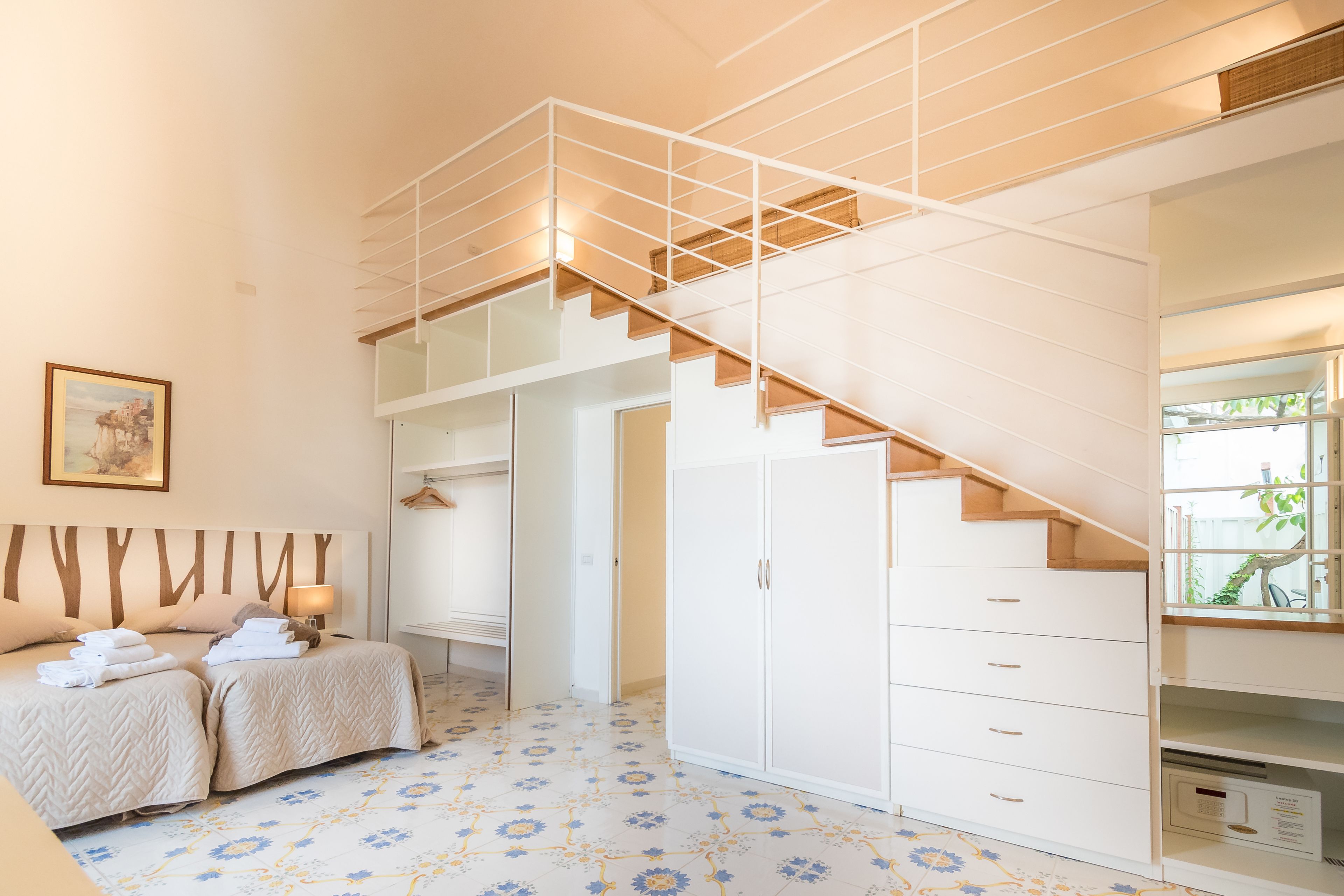 A hotel room with two beds, a staircase, a wardrobe, and a painting on the wall.