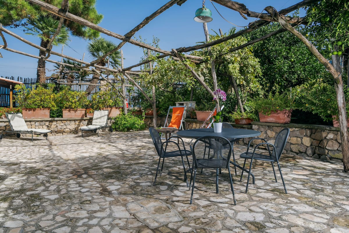 An outdoor patio with stone flooring, metal chairs, a table, and potted plants.