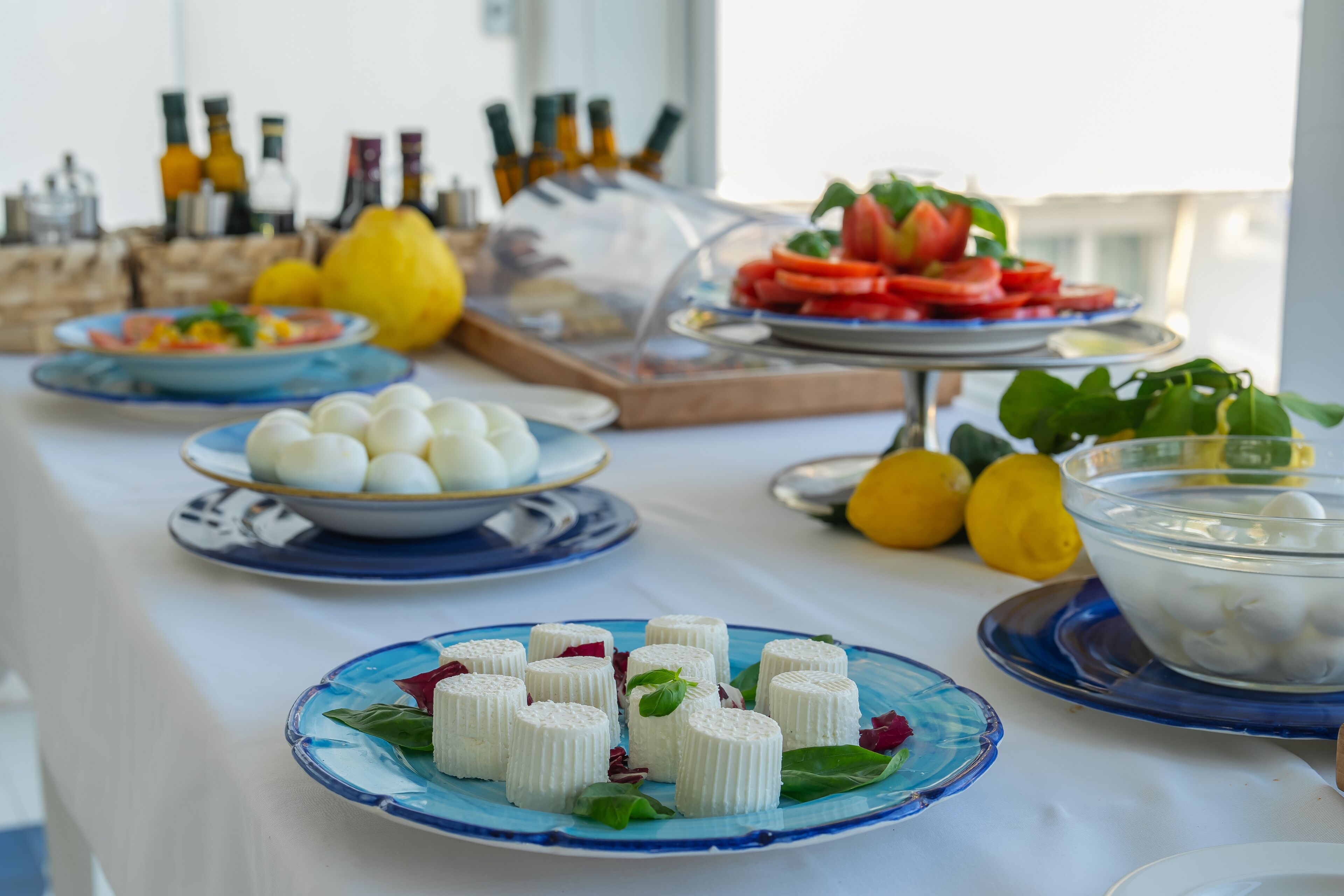 A buffet table with various dishes including cheese, tomatoes, and lemons.