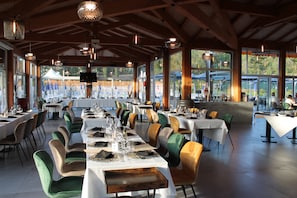 Ein Restaurant mit mehreren Tischen, großen Fenstern und Blick ins Freie.