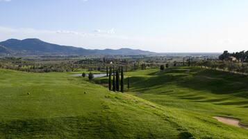A golf course with rolling hills, a pond, and distant mountains.
