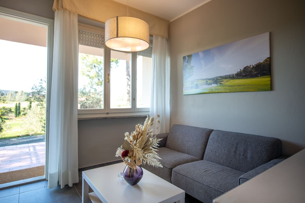 Un salón con un sofá gris, una mesa de centro blanca y un jarrón con plantas secas.