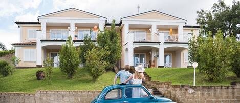 Una casa de dos pisos con un balcón y un coche pequeño estacionado adelante.