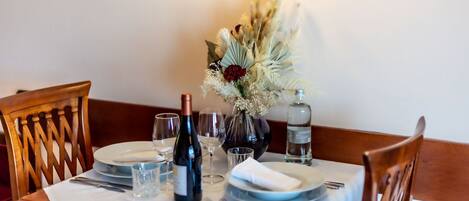 Una mesa de comedor dispuesta con platos, cubiertos, copas de vino y un florero con flores secas.