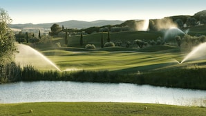 Un campo de golf con un estanque, árboles y colinas al fondo.