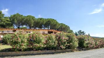 A building with a tiled roof, surrounded by flowering bushes and trees.