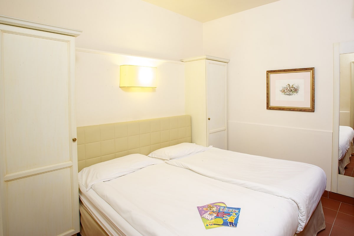 Une chambre d’hôtel avec un lit double, une lampe de chevet, un tableau encadré au mur et une porte sur le côté gauche.