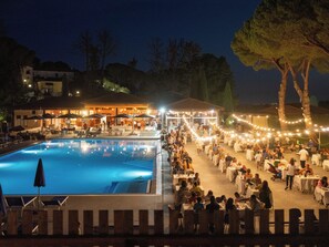 Un espace extérieur avec une piscine, des tables et des chaises, entouré d’arbres et de bâtiments.
