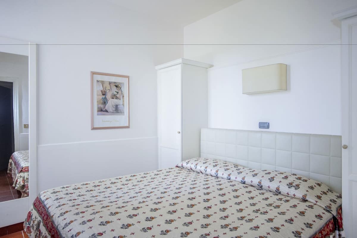 Ein Schlafzimmer mit einem Bett, einem gerahmten Bild, einem Spiegel und einer Tür.