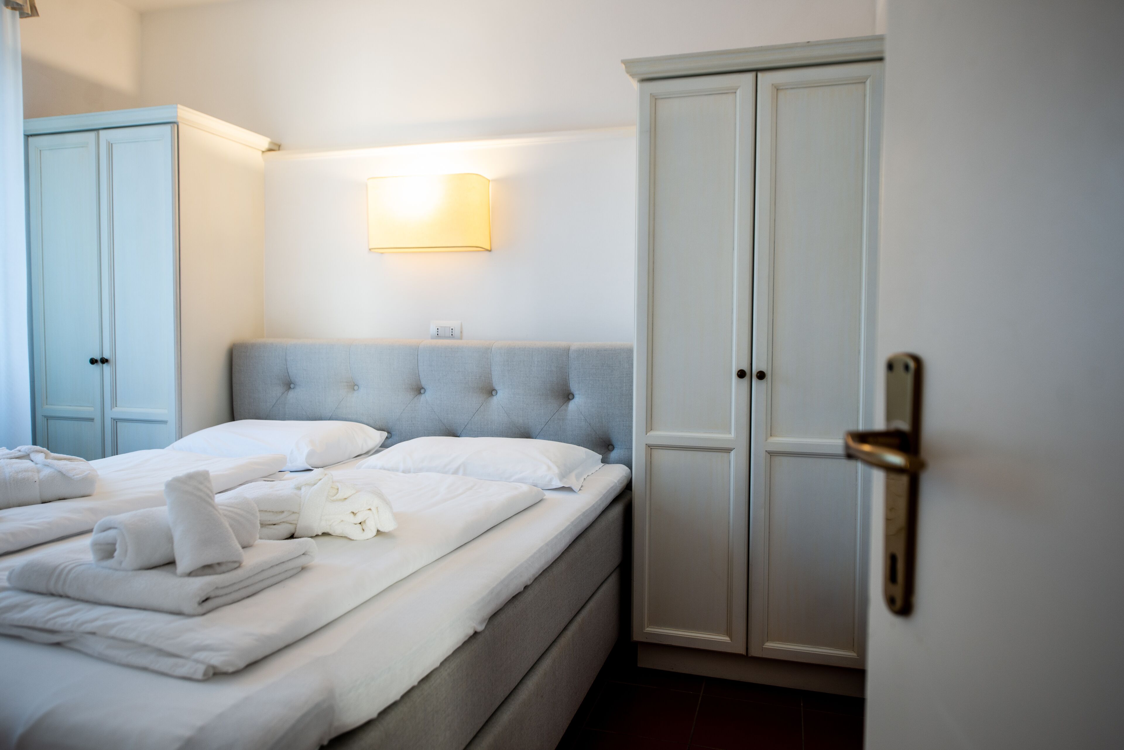 A neatly made bed with white linens and towels, a tufted headboard, and a wardrobe with a door handle.
