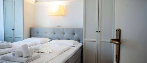 A neatly made bed with white linens and towels, a tufted headboard, and a wardrobe with a door handle.