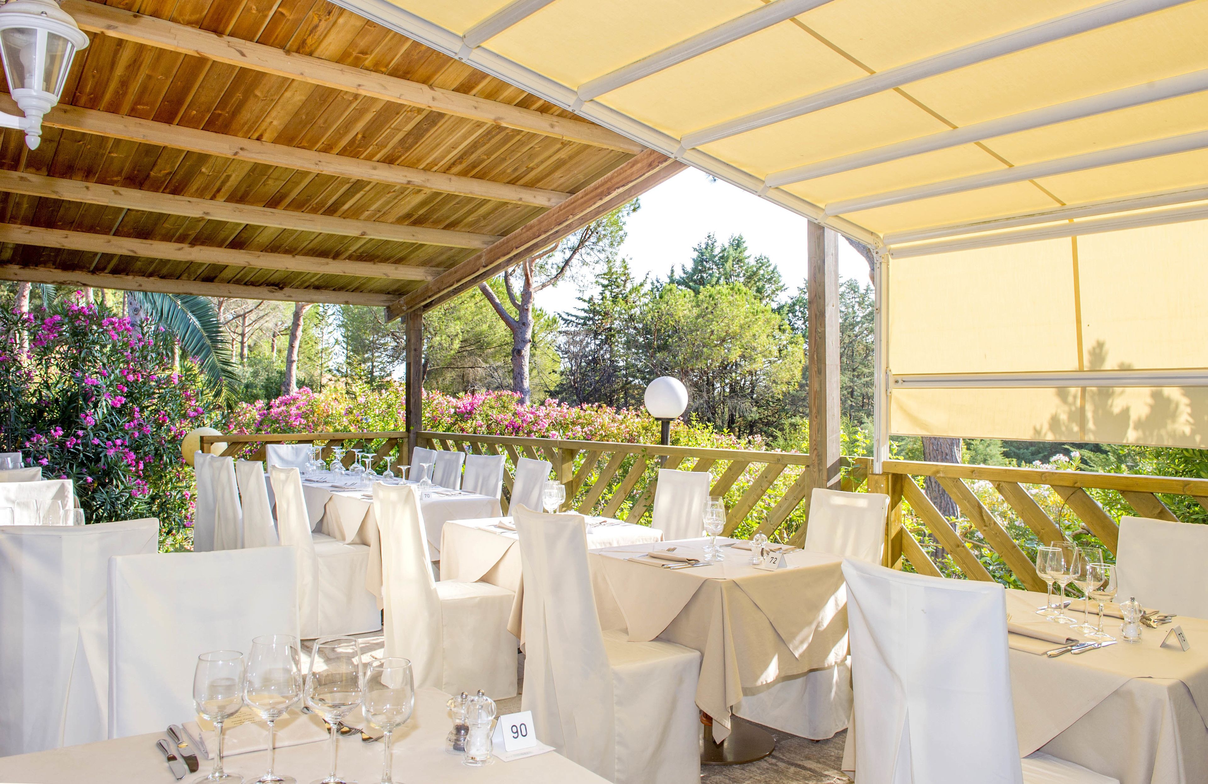 An outdoor restaurant with tables set for dining, covered by a wooden roof and white canopies.