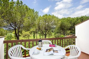 Un balcon avec des chaises blanches, une table, une cafetière, une tasse, un livre et un croissant.