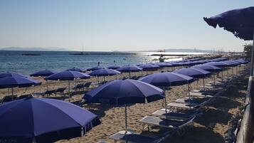 Ein Strand mit Liegestühlen und Sonnenschirmen, ein klarer Himmel und ruhiges Meer.
