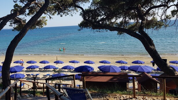 Una playa con sombrillas azules y una terraza de madera.