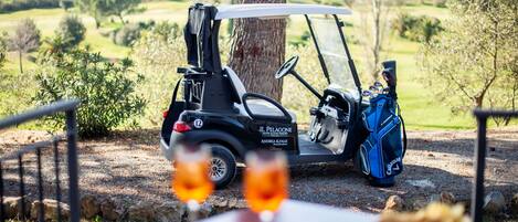 A golf cart parked near a table with two glasses of wine and a plate of food, with a scenic view of a golf course in the background.
