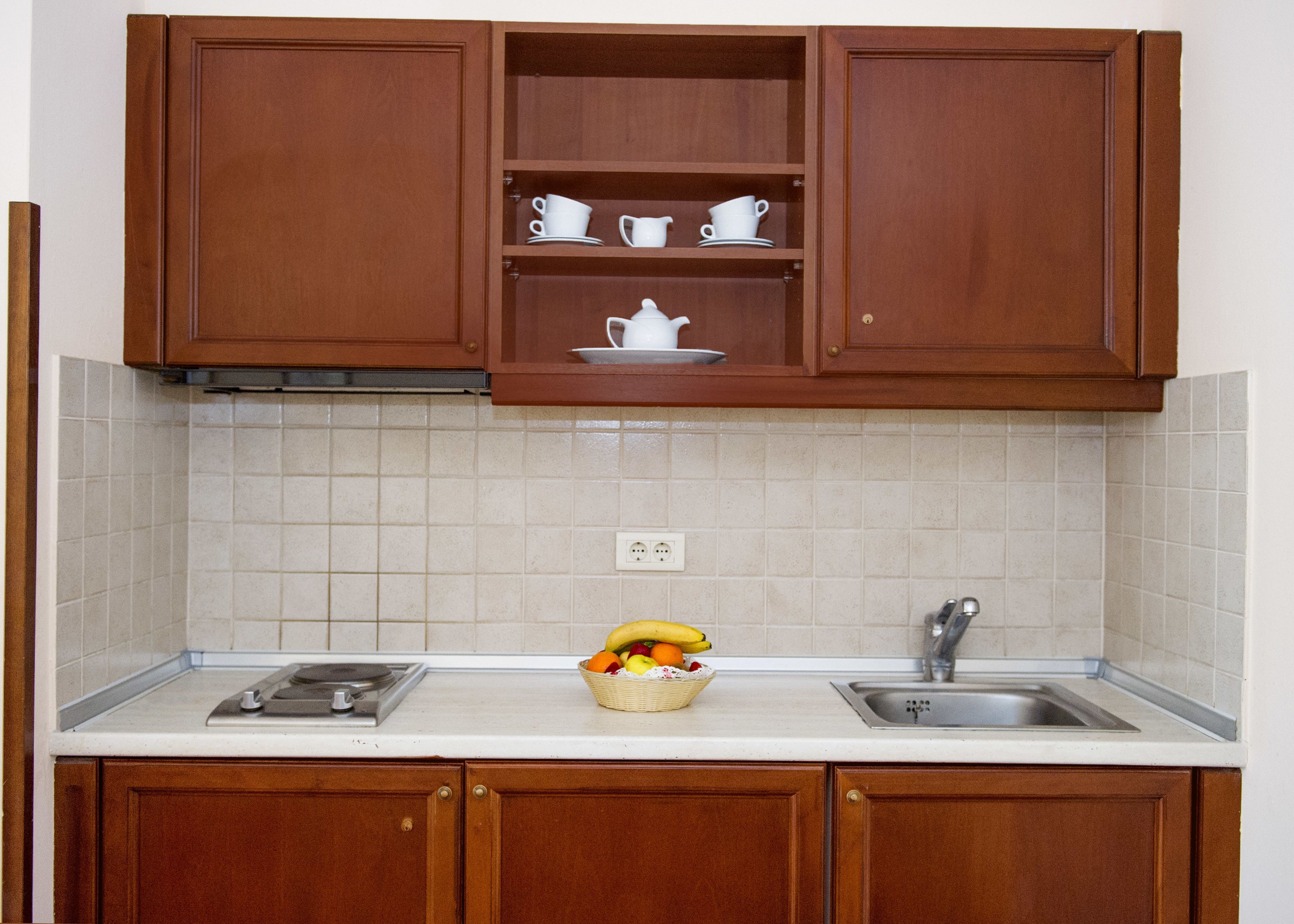 Una cocina con armarios de madera, encimera blanca, un fregadero y una cesta de frutas.