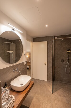 Une salle de bain moderne avec un grand lavabo ovale, un miroir rond, un espace douche et un meuble-lavabo en bois.