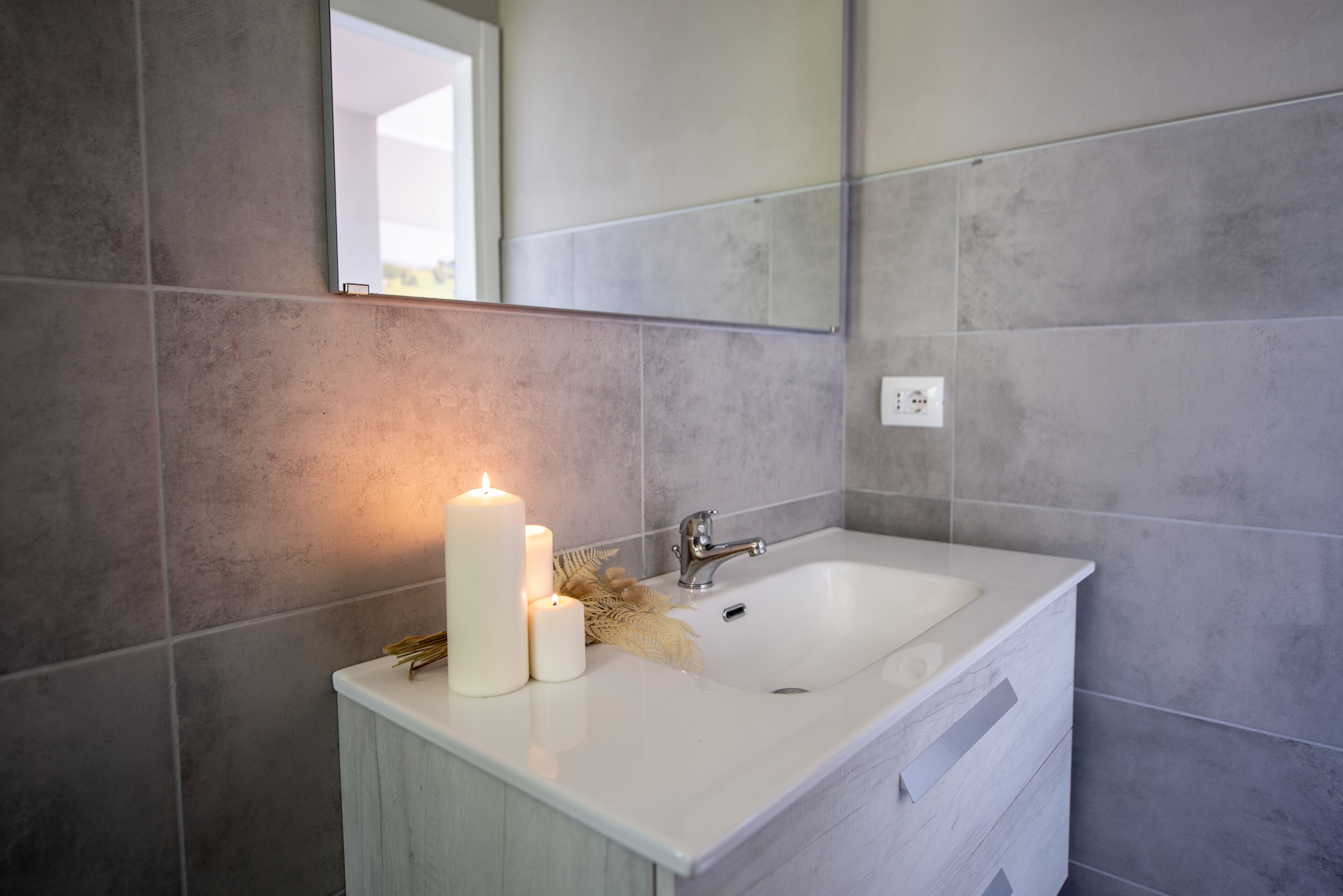 Une salle de bain avec un lavabo blanc, deux bougies et un miroir au-dessus.
