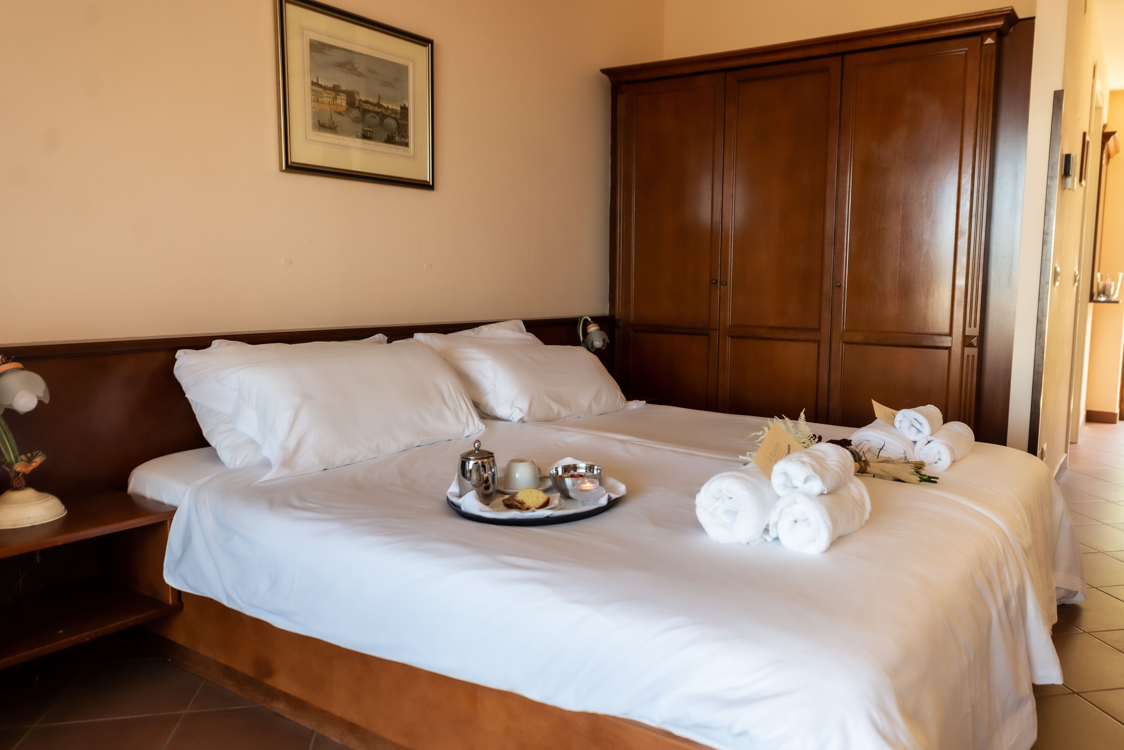 A neatly made bed with white linens, a tray with breakfast items, and rolled towels.