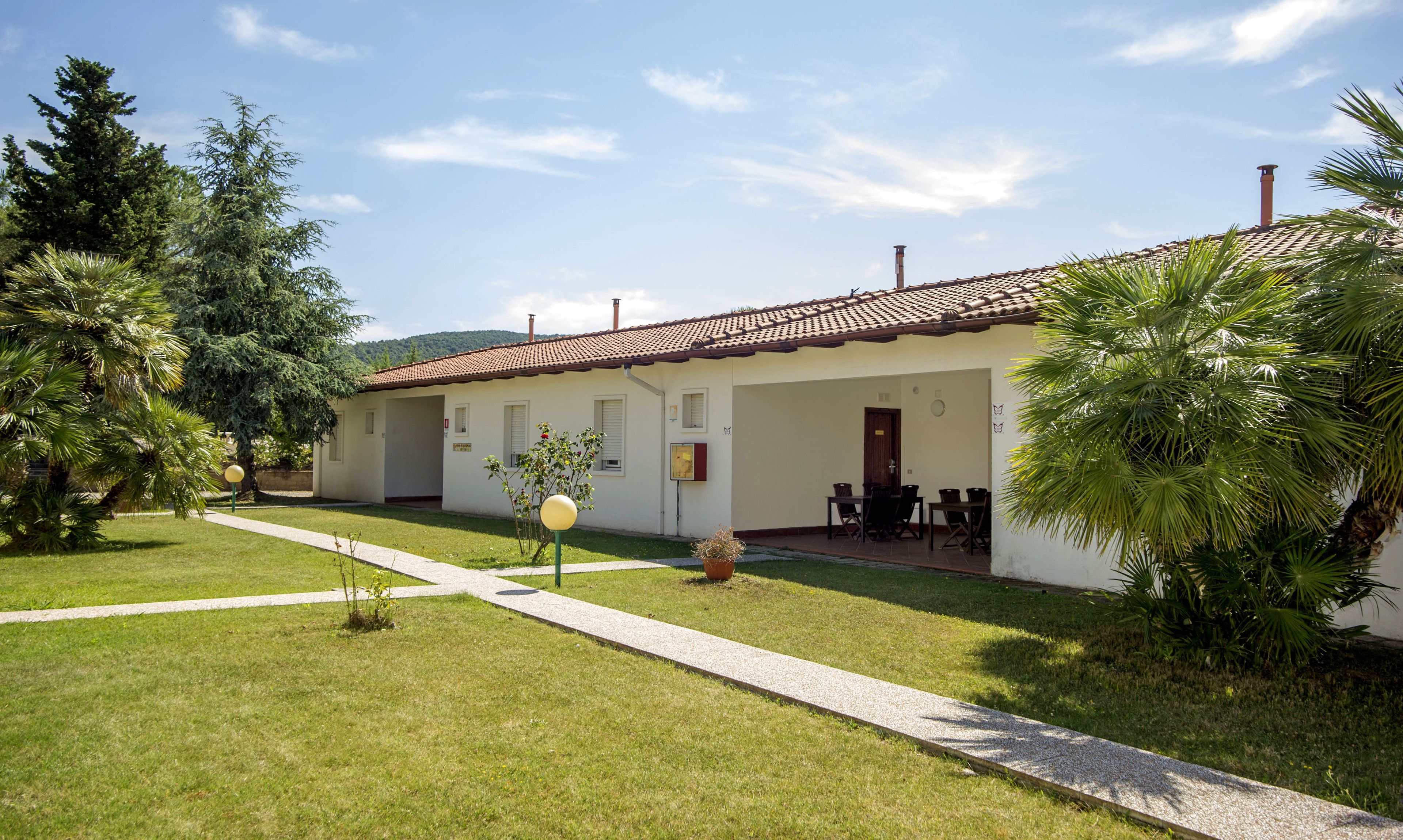 A single-story house with a tiled roof, a covered patio with outdoor furniture, and a well-maintained lawn.
