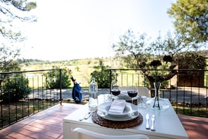 A table set for two with a view of a rural landscape, a bottle of water, wine glasses, and a vase with flowers. - Il Pelagone Hotel & Golf Resort Toscana (Gavorrano)