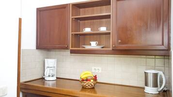 Una cocina con armarios de madera, una cafetera, una cesta de fruta y un hervidor.