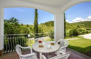 Un balcon avec une table dressée pour le petit-déjeuner, offrant une vue sur un paysage verdoyant et luxuriant, parsemé d’arbres et de collines.