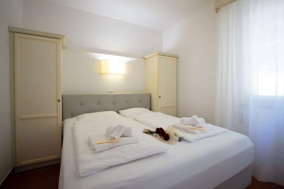 Ein Doppelbett mit weißen Bettwäsche, ein grauer Kopfteil und eine Wandleuchte.