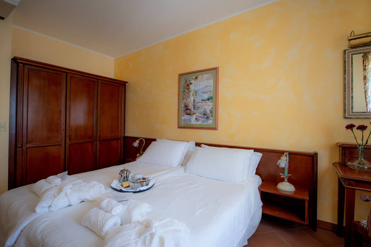 Habitación de hotel con una cama grande, un armario de madera, un cuadro en la pared y una pequeña mesa con flores.