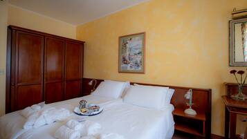Habitación de hotel con una cama grande, un armario de madera, un cuadro en la pared y una pequeña mesa con flores.