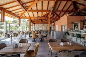 Un vaste espace de restauration intérieur, doté de hauts plafonds et de poutres en bois, et comprenant de nombreuses tables et chaises.