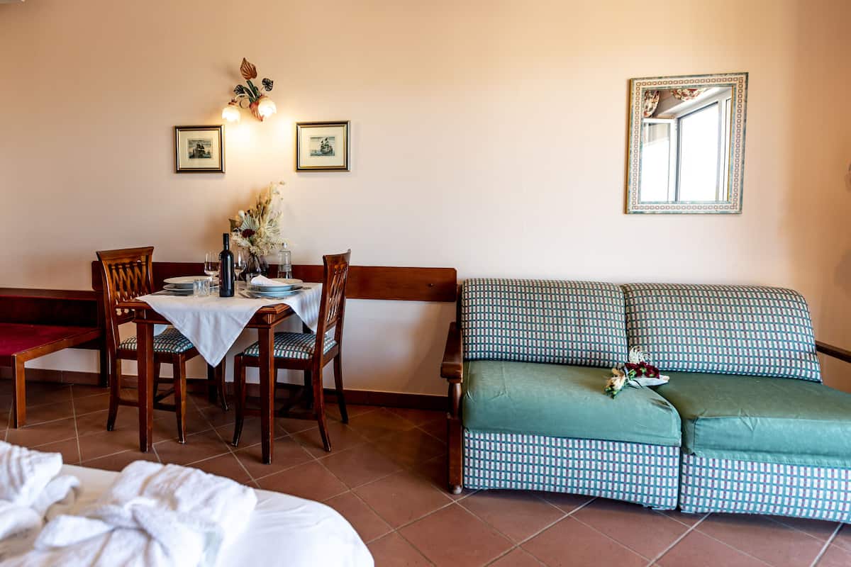 Un comedor con una mesa dispuesta para cuatro, dos sillas, un sofá y un espejo en la pared.
