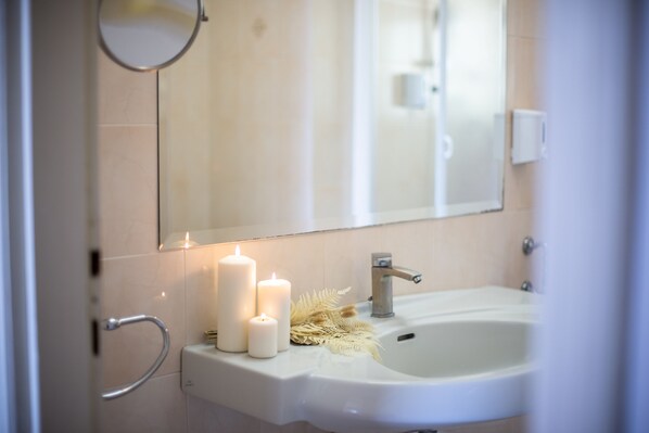 Ein Badezimmer mit einem weißen Waschbecken, zwei brennenden Kerzen und einem Spiegel.