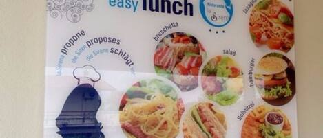 A menu board with various lunch options including bruschetta, salad, hamburger, carbonara, and club sandwich.