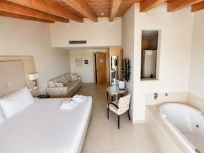 Ein Hotelzimmer mit einem großen Bett, einem Sofa, einem kleinen Tisch, einem Sessel, einem Fernseher und einer Badewanne.
