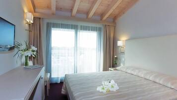 Et hotelværelse med seng, skrivebord, fjernsyn og et vindue med gardiner.