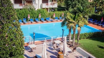 Zona de piscina con sillas reclinables azules, una palmera y un edificio con balcones.