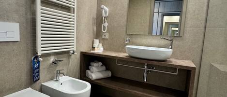 A modern bathroom with a large mirror, two sinks, a bidet, and a towel rack.