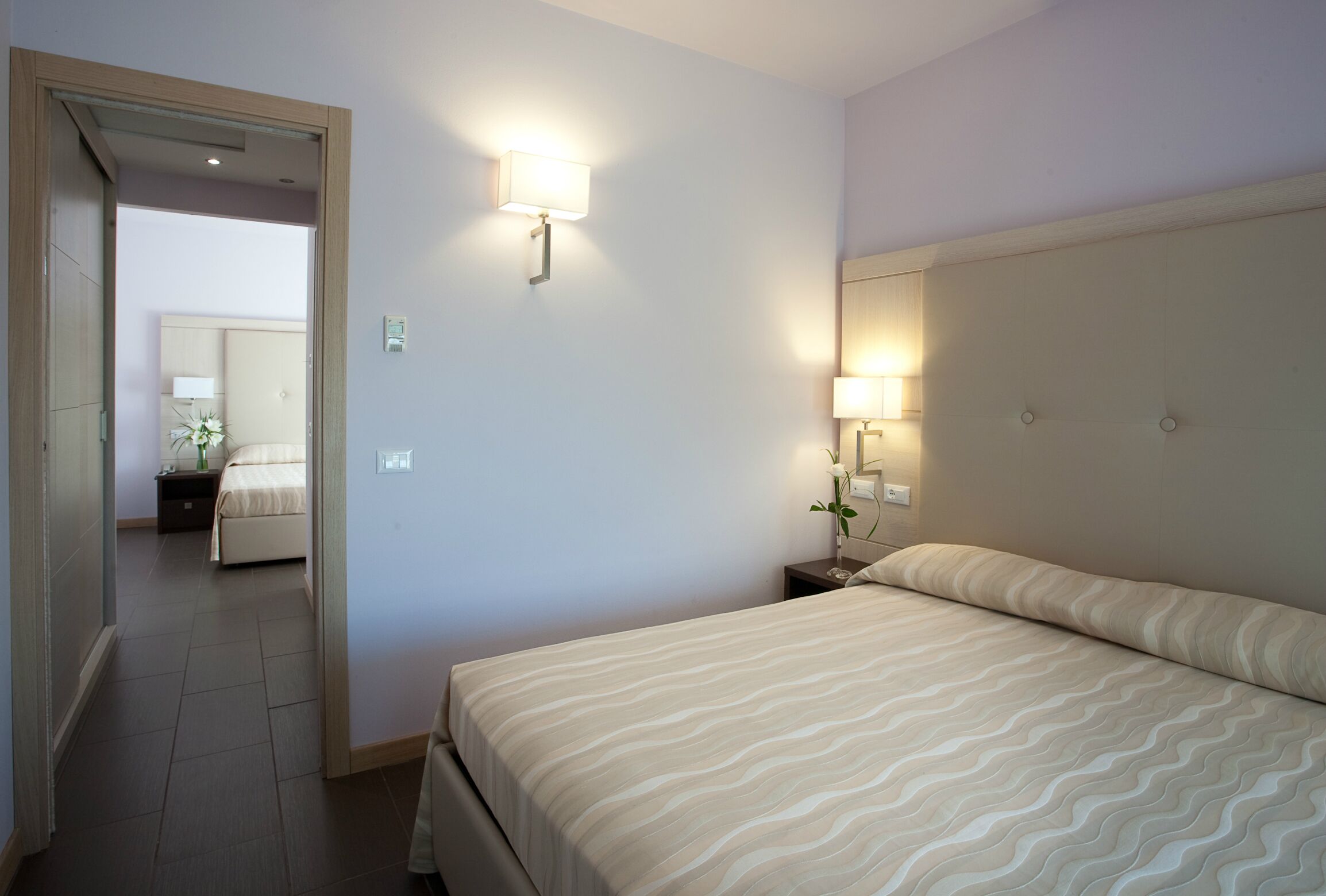 Una habitación de hotel con cama, lámparas de noche, mesita de noche y espejo.