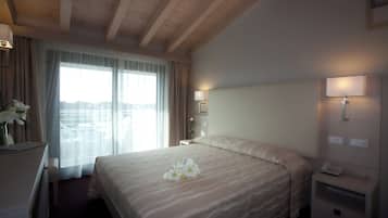 Una habitación de hotel con una cama grande, una mesita de noche con lámpara, un teléfono en la mesita y una ventana con cortinas.