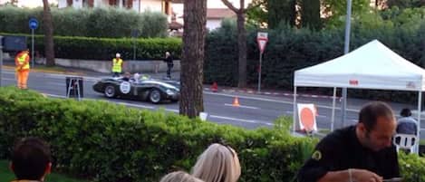Un área al aire libre con carpa, una mesa preparada para comer, un árbol y un camino con un coche y una persona con chaleco reflectante.