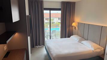 Une chambre d’hôtel équipée d’un lit, d’un bureau, d’une chaise, d’une lampe et offrant une vue sur une piscine.