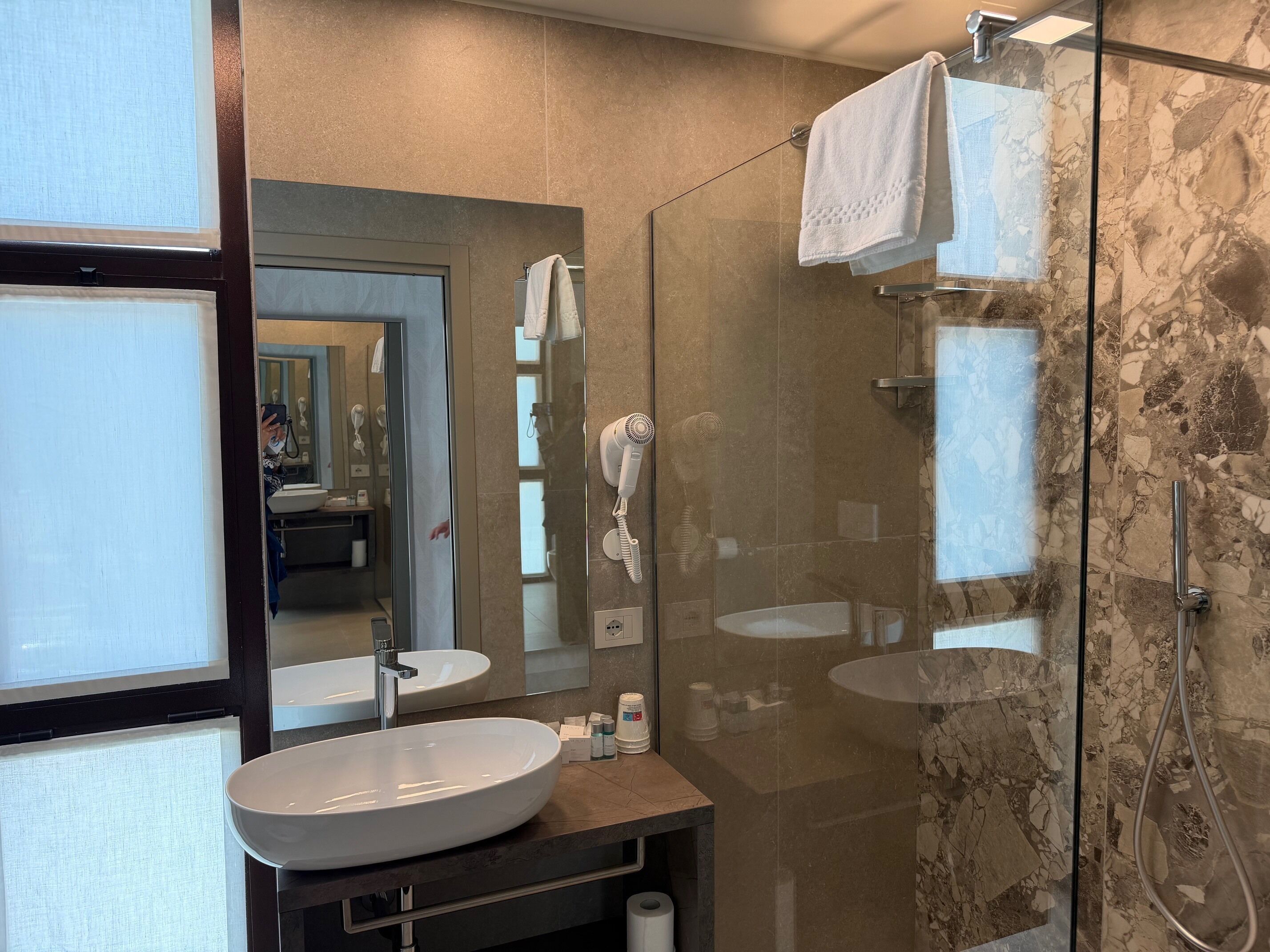A modern bathroom with a glass-enclosed shower, a large mirror, and a round sink.