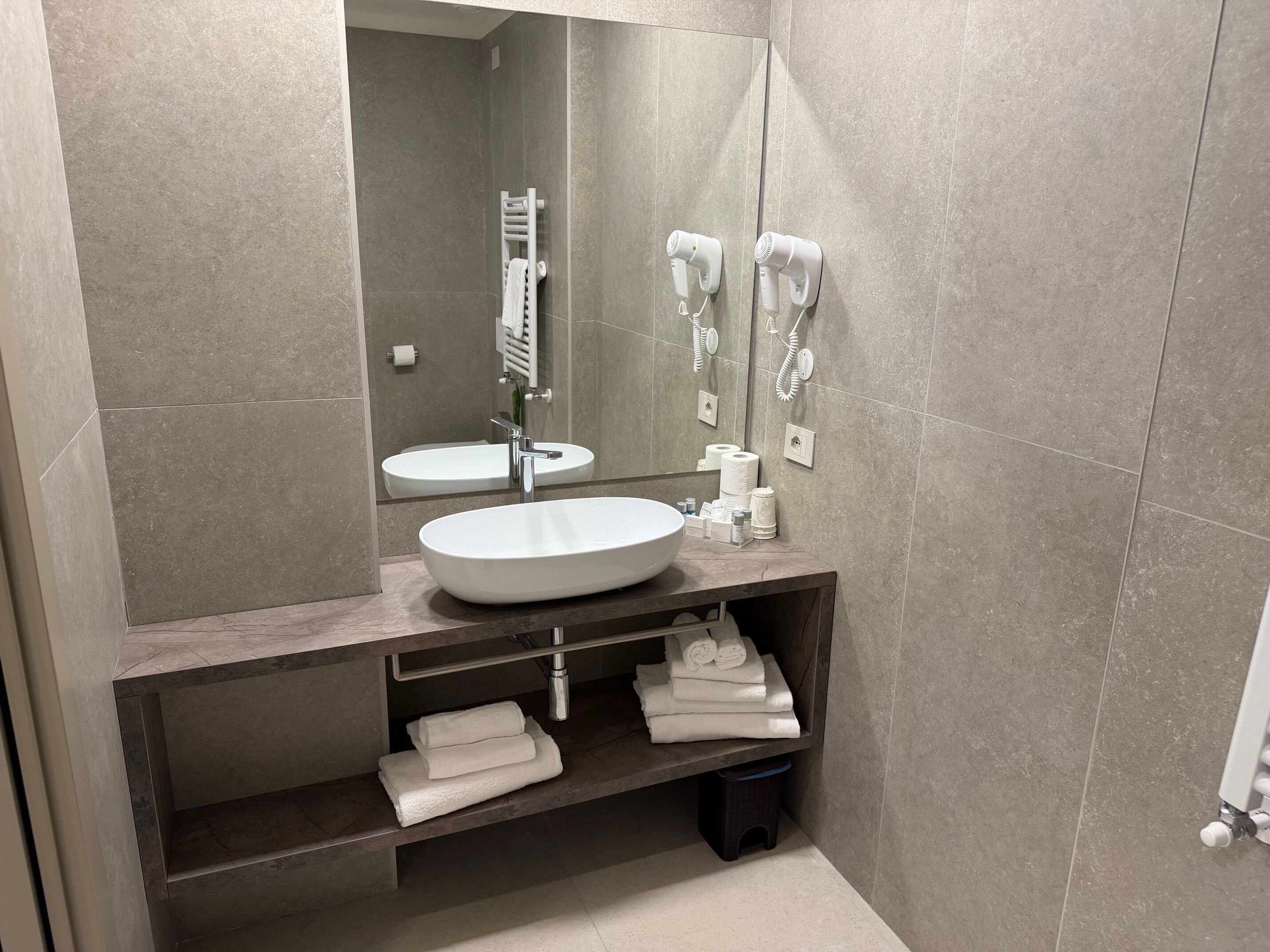 A modern bathroom with a large mirror, a sink, a towel rack, and a hairdryer.