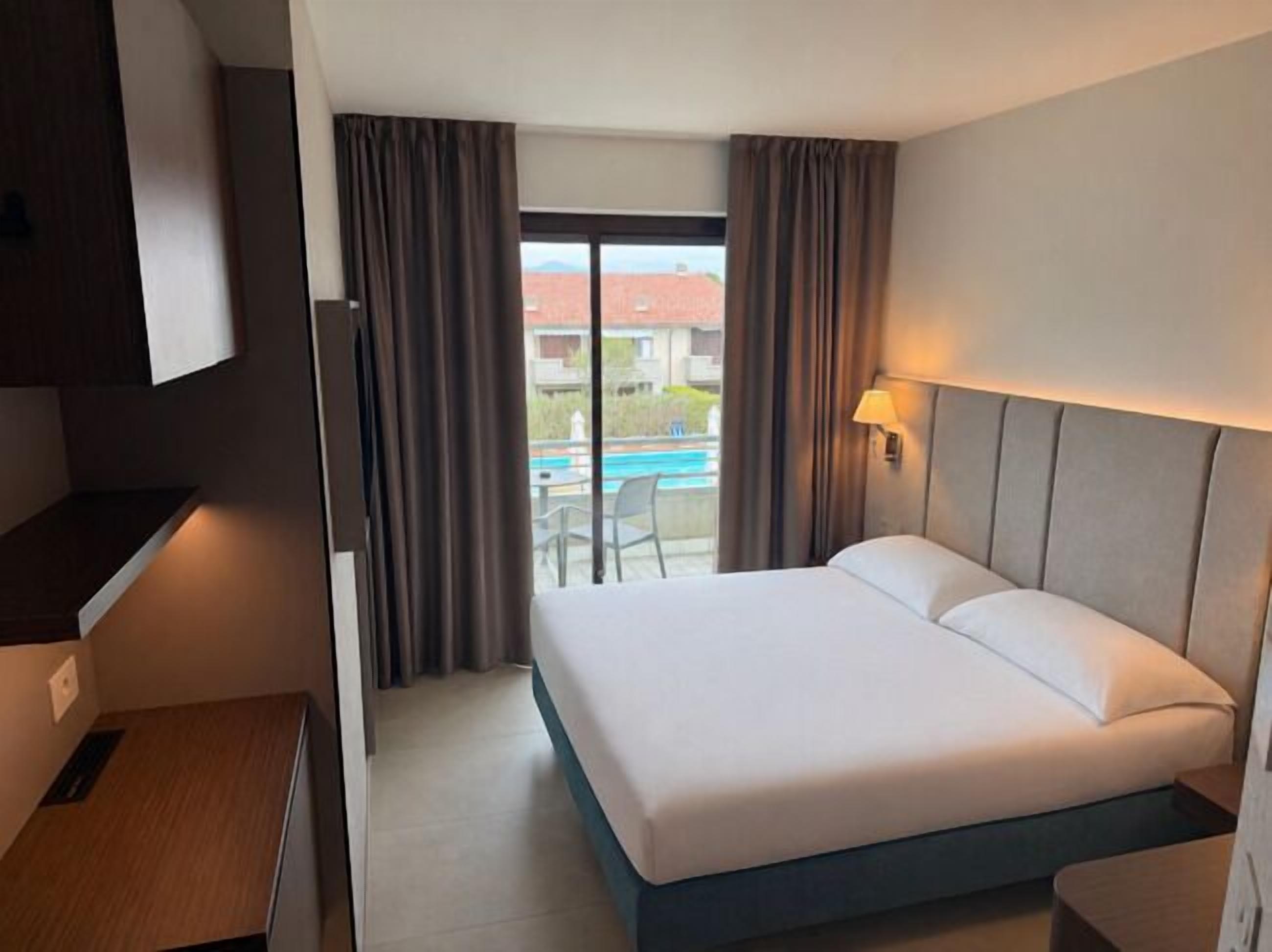 Une chambre d’hôtel avec un lit, un bureau, une lampe et une vue sur une piscine.
