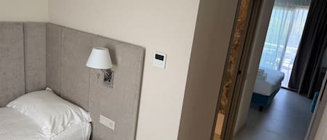 Et hotelværelse med seng, lille bord, vægmonteret lampe, digitalt ur og udsigt ud af vinduet.