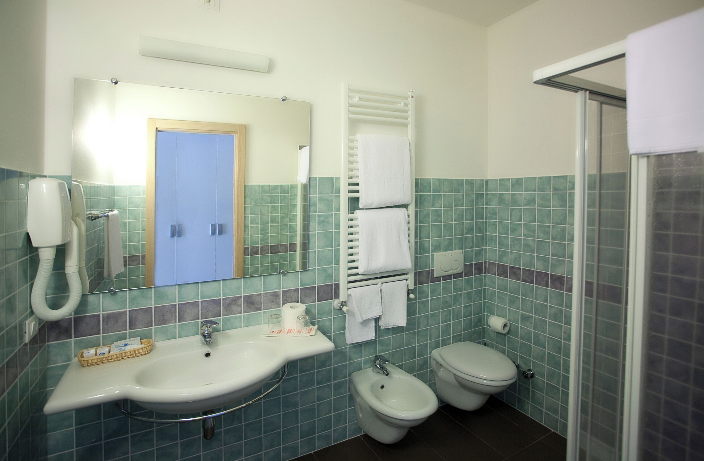 Ein Badezimmer mit Waschbecken, zwei Toiletten, einem Bidet, einem Handtuchhalter und einer Dusche.