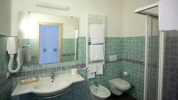 Een badkamer met een wastafel, twee toiletten, een hygiëneschuimer, een handdoekhouder en een douchegedeelte.